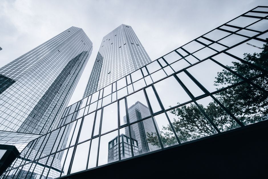 Imagem de arranha-ceus modernos refletindo o céu nublado, simbolizando o ambiente corporativo e o universo dos negócios.