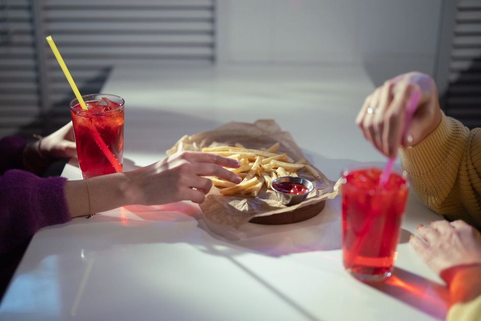 duas pessoas compartilhando batatas fritas e refrigerantes em um ambiente descontraído, promovendo convivência social e lazer