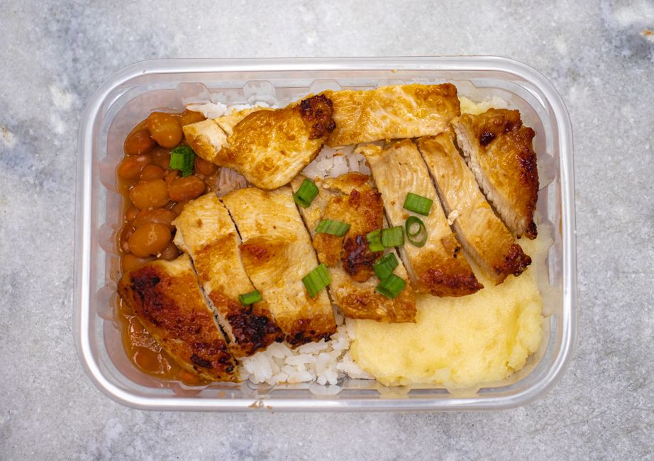 Imagem de um pote de marmita com arroz, frango grelhado, feijão, purê de batata e alimentos preparados para refeição rápida ou almoço para levar.