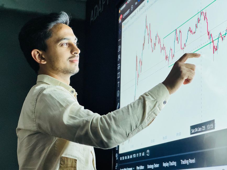 Homem analisando gráficos de mercado financeiro em ambiente de escritório, ilustrando temas de investimentos e estratégias de negociação.