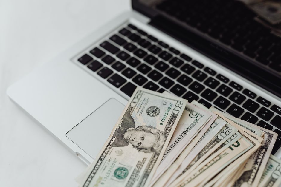 Imagem de um laptop com uma pilha de dinheiro, simbolizando temas de finanças, investimentos ou economia digital.