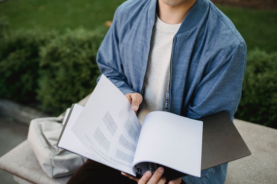 Homem sentando em ambiente ao ar livre, lendo um caderno com gráficos, ilustrando temas de análise de dados ou estudos ao ar livre.