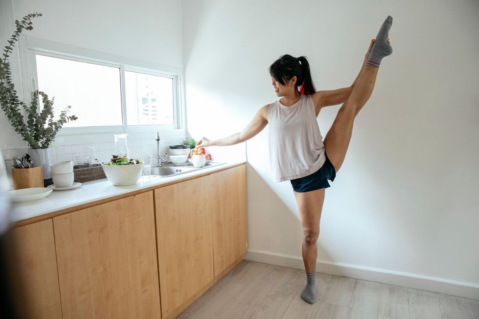 Jovem praticando alongamento ou exercício de flexibilidade na cozinha em casa, promovendo bem-estar e saúde.