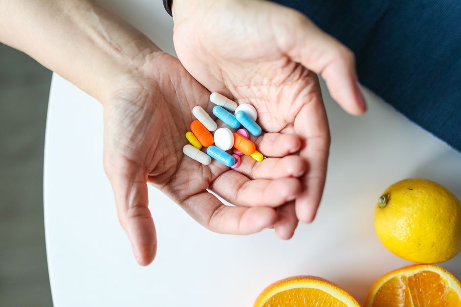 Uma pessoa segurando um punhado de medicamentos coloridos em uma mesa com limões ao lado, representando saúde, medicação e bem-estar.