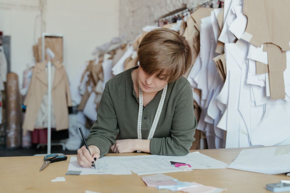 Designér ou costureira concentrada trabalhando em projetos de moda em um ateliê organizado com moldes e papéis. 