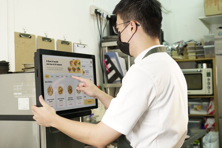 Pessoa utilizando um sistema de pagamento digital em um ambiente de cozinha profissional, destacando a tecnologia na gestão de pedidos.