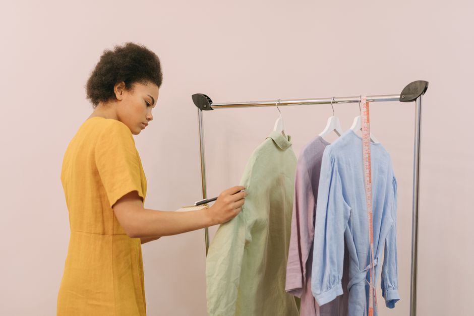 Mulher analisando roupas em um cabideiro, representando escolhas e estilo na moda.