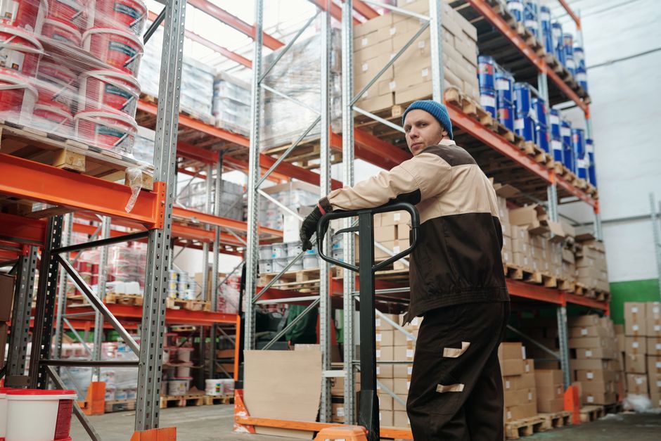 Homem em armazém industrial organizando estoque de produtos com foco em logística e distribuição.