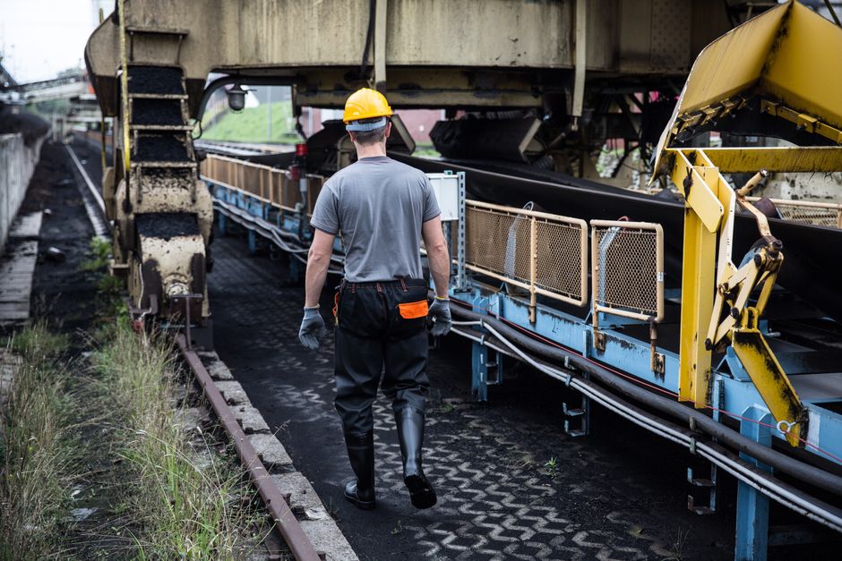 Um técnico ou engenheiro em inspeção de obras ferroviárias, observando uma máquina de transporte de materiais na linha de trem.