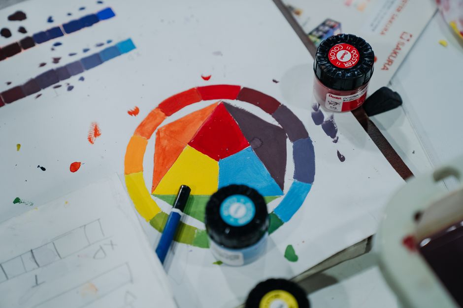 Uma paleta de cores vibrantes sendo explorada em um projeto artístico, com tintas e pincéis sobre uma superfície de papel.