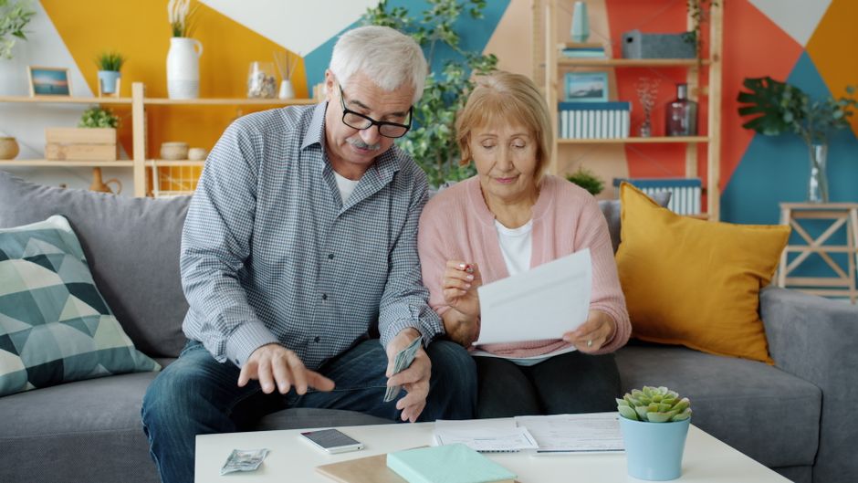 Casal de idosos analisando documentos financeiros em ambiente acolhedor, simbolizando planejamento financeiro na terceira idade.