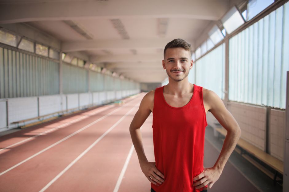 Atleta em postura de confiança em uma pista de corrida coberta, representando dedicação e preparação esportiva.