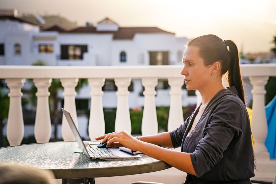 Mulher trabalhando com laptop em varanda ao entardecer, simbolizando produtividade e trabalho remoto.