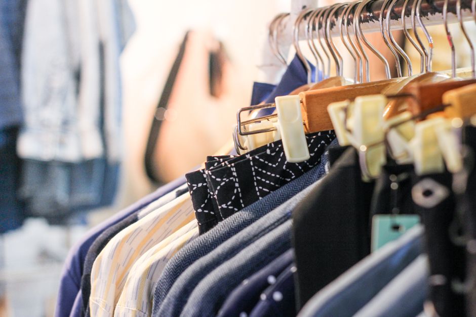 Imagem de cabides com roupas variadas penduradas em uma loja, representando comércio de vestuário e moda.