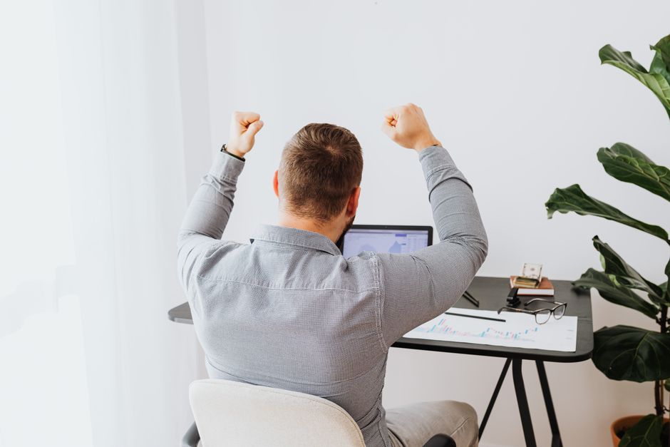 Homem comemorando uma conquista no trabalho, demonstrando entusiasmo e satisfação com o sucesso profissional.