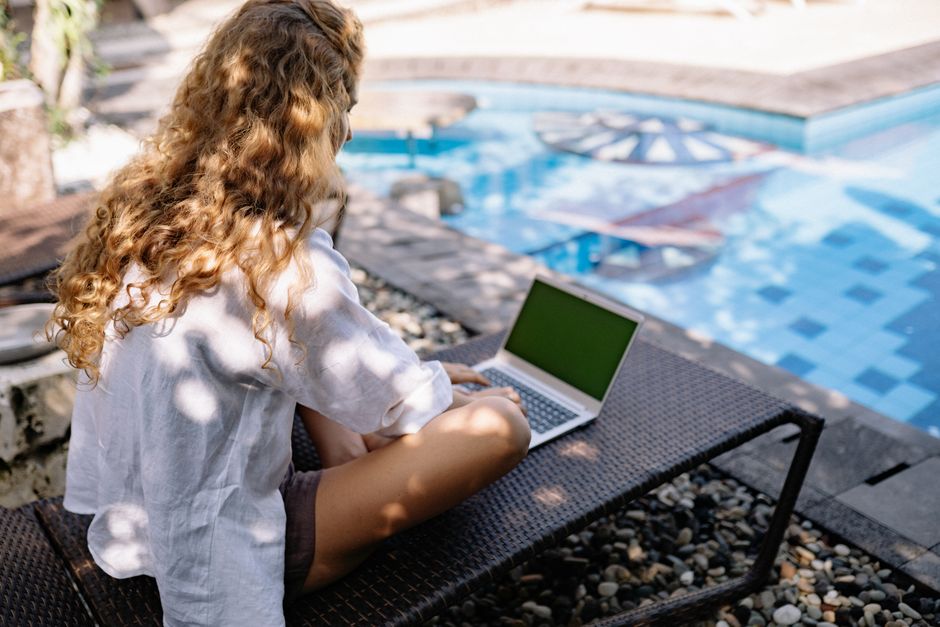 Mulher usando laptop ao lado da piscina, simbolizando trabalho remoto ou lazer digital ao ar livre.