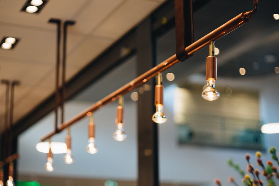 Luminárias modernas instaladas no teto de um espaço de convivência ou café, criando uma atmosfera acolhedora e contemporânea.