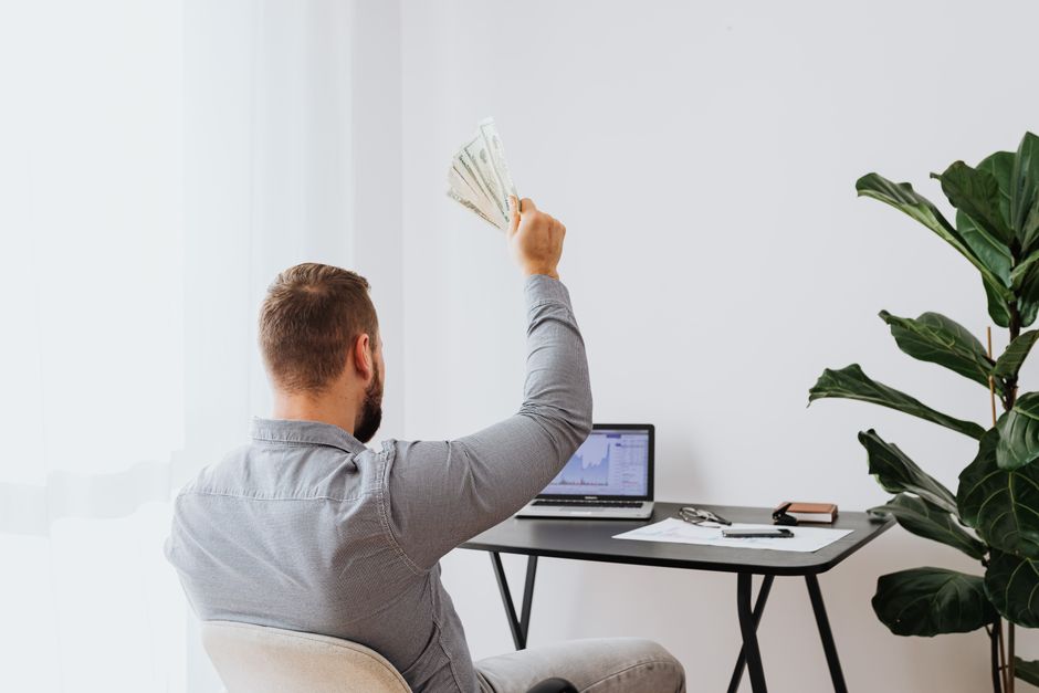 Homem celebrando o sucesso financeiro enquanto trabalha em um ambiente de escritório com um laptop exibindo gráficos