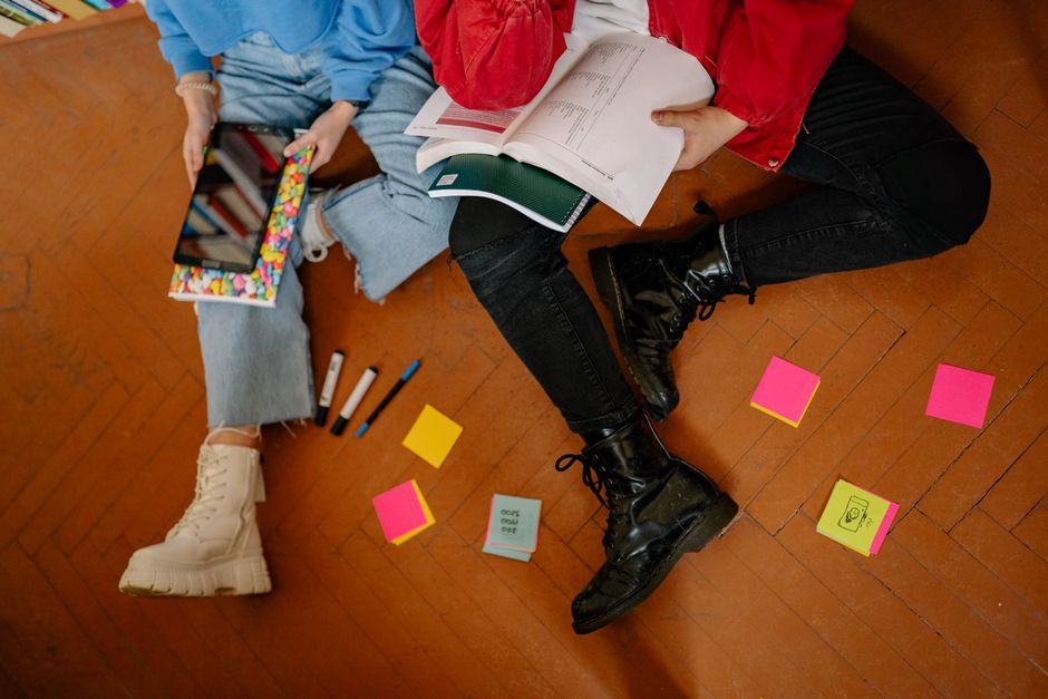 Duas pessoas estudando e discutindo em um ambiente informal, com materiais de estudo e elementos visuais organizados.