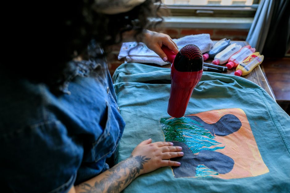 Pessoa usando um secador de cabelo para criar uma arte texturizada em uma camiseta pintada à mão.