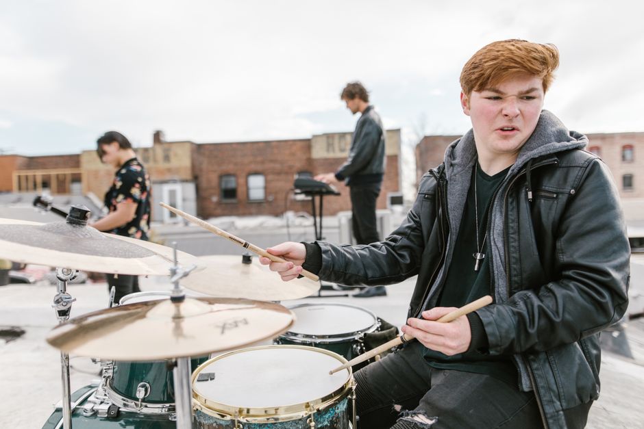 Jovem tocando bateria em um espaço ao ar livre, representando paixão pela música e prática artística.