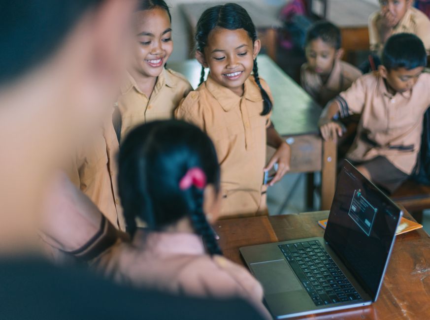 Crianças em sala de aula interagindo com um computador, promovendo o ensino de tecnologia na educação infantil.