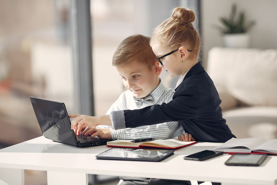 Crianças estudando juntas com tecnologia e materiais escolares em ambiente indoor, simbolizando aprendizagem e colaboração.