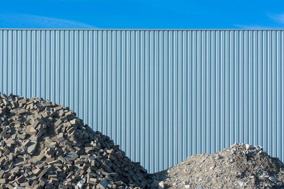 Imagem de um muro de metal com pilhas de blocos de concreto ao seu pé, representando construção ou infraestrutura industrial.
