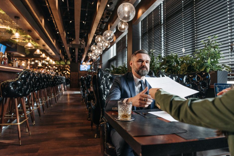 Homem de negócios sério participando de uma reunião em um ambiente moderno de café ou restaurante, transmitindo profissionalismo e networking.