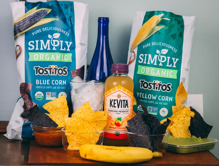 Imagem de um lanche saudável com chips orgânicos, bebida probiótica e frutas, ideal para um artigo sobre alimentação balanceada ou snacks naturais.