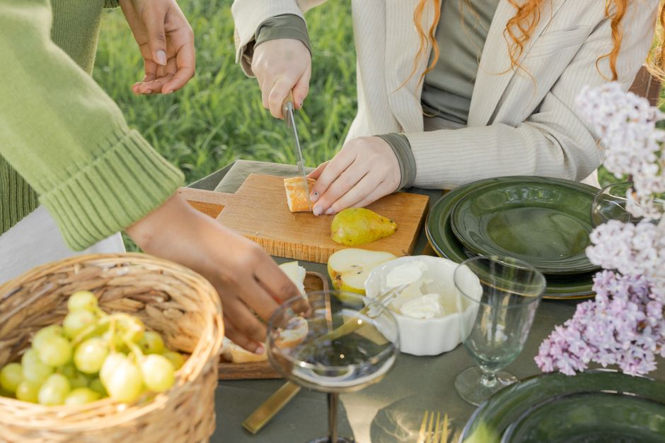 Pessoas preparando comida ao ar livre em um ambiente natural, com frutas e pratos para refeição.