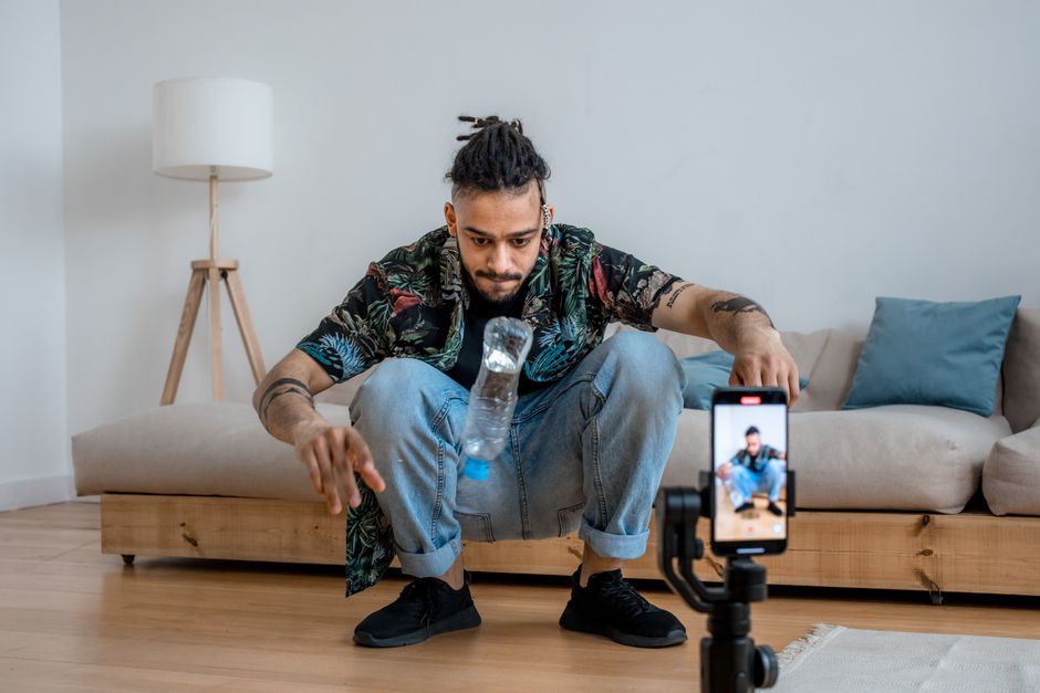 Homem realizando um treino de equilíbrio e coordenação em casa, enquanto grava um vídeo para redes sociais ou canal de conteúdo digital.