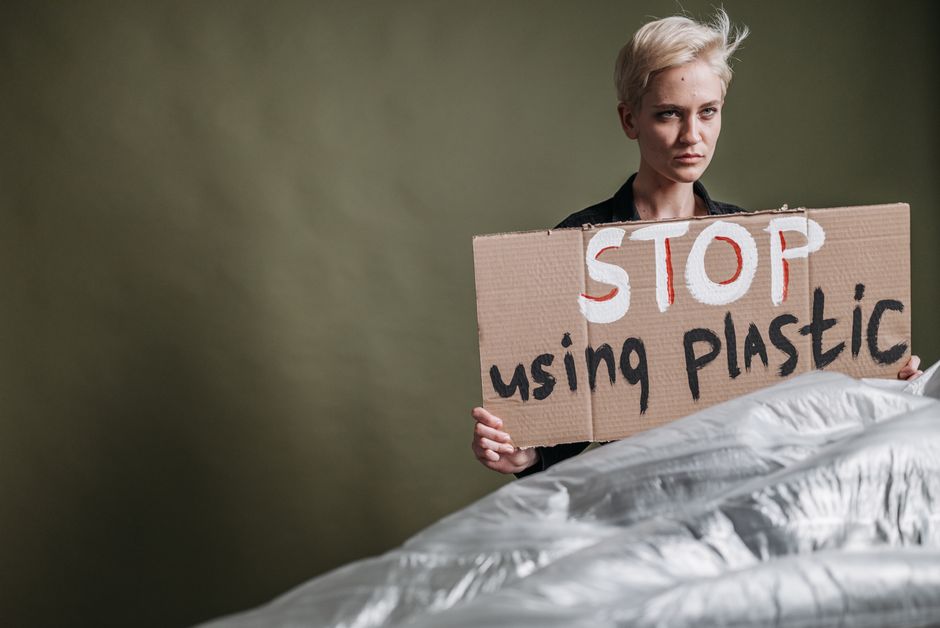 Mulher protestando contra o uso de plástico, segurando um cartaz com a mensagem de conscientização.