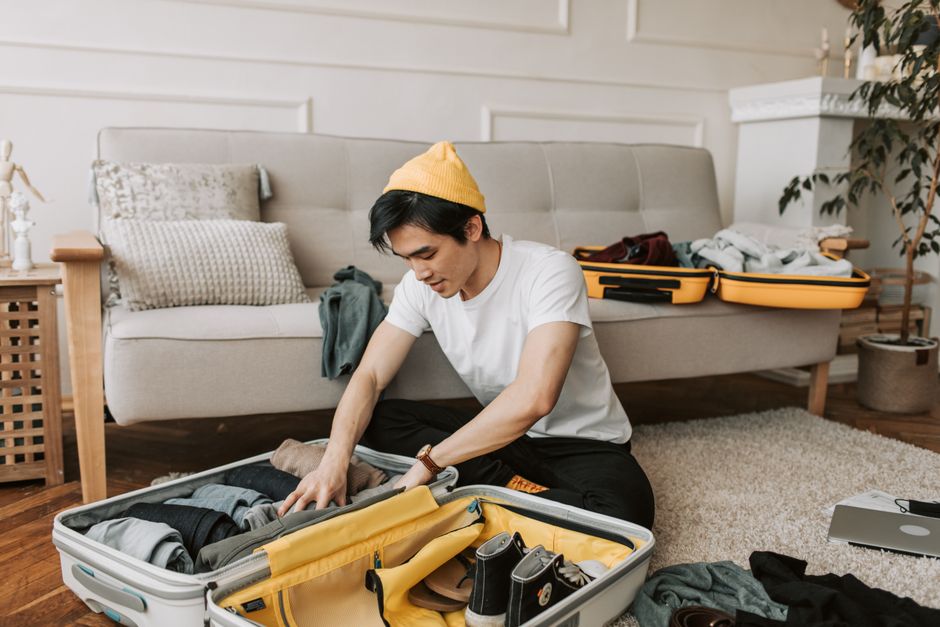 Jovem organizando uma mala em casa, preparando-se para uma viagem ou mudança.