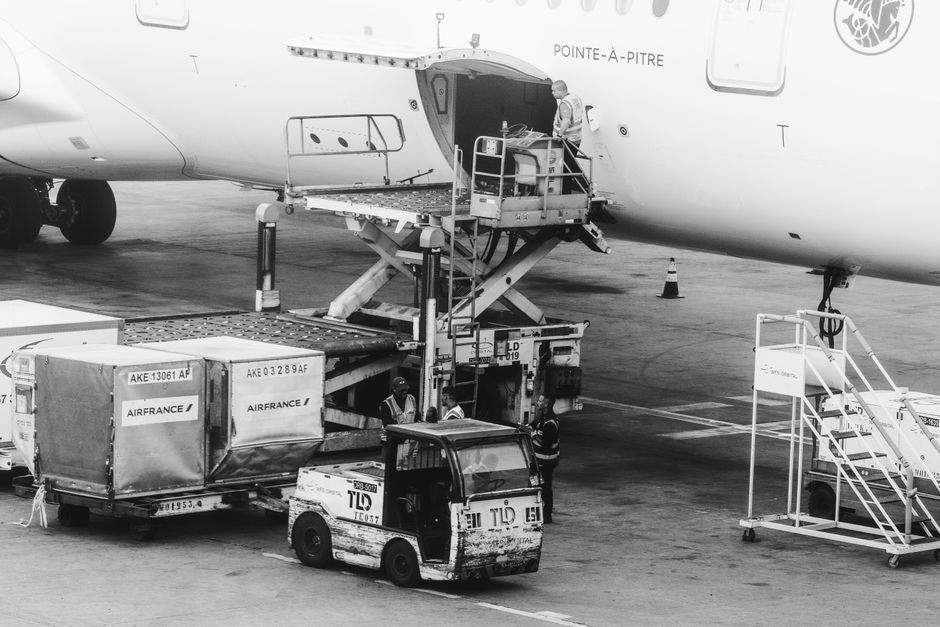 Imagem de uma operação de carga e descarga de um avião em um aeroporto, destacando atividades logísticas e transporte de cargas aéreas.