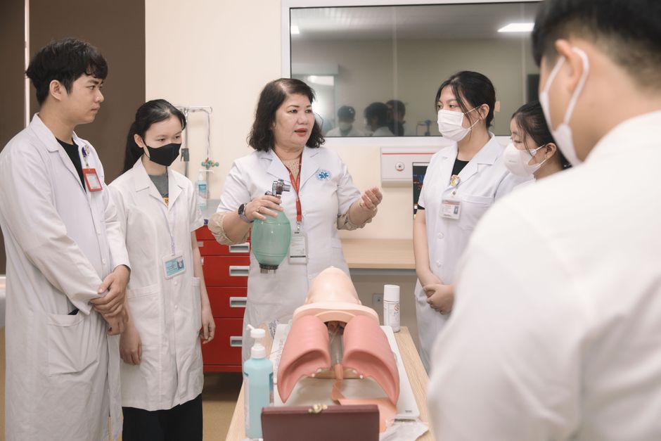 Grupo de estudantes de Medicina participando de aula prática sobre anatomia respiratória sob orientação de professora em um ambiente de ensino.