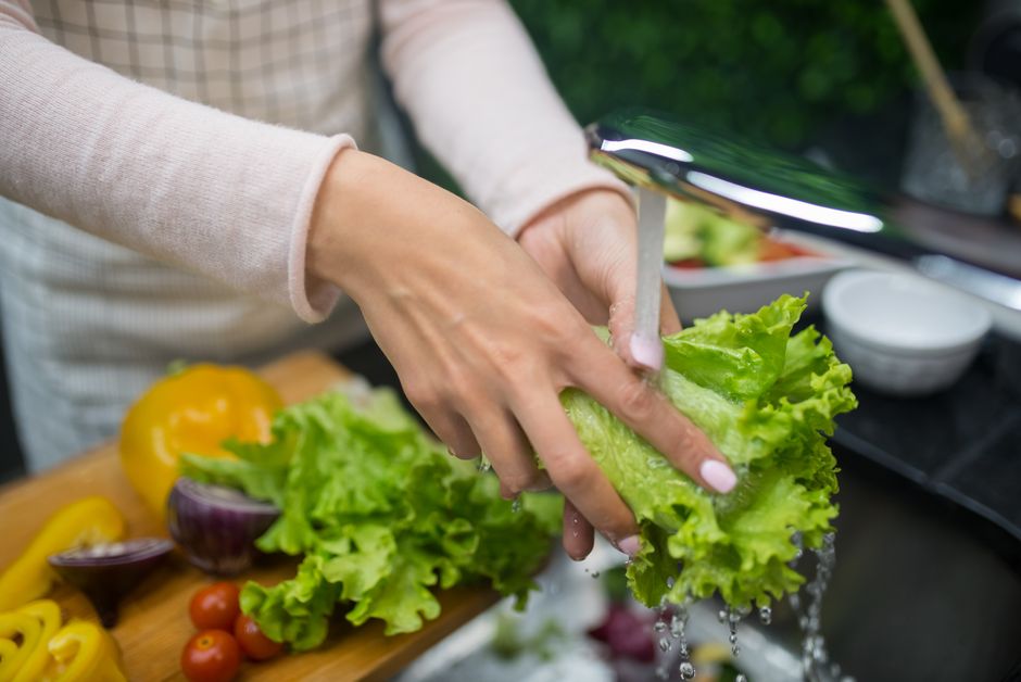 Pessoa lavando folhas de alface em uma cozinha ao ar livre, destacando a preparação de alimentos frescos para uma receita saudável.