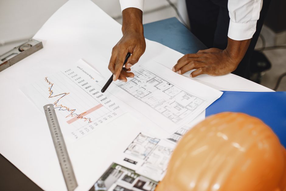 Profissional analisando plantas e dados financeiros em um ambiente de escritório, simbolizando planejamento e projetos de construção ou arquitetura.