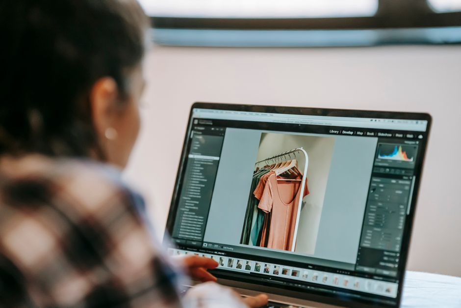Pessoa editando fotos de roupas em um laptop, ilustrando criatividade no e-commerce de moda.