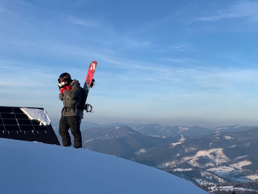 Pessoa preparando-se para esquiar no topo de uma montanha com uma vista panorâmica de paisagens nevadas ao fundo.