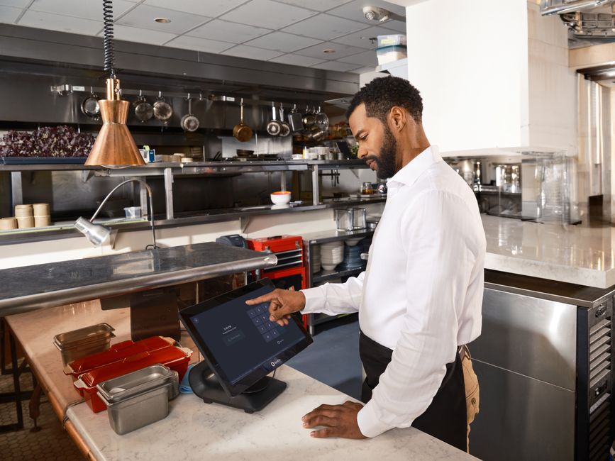 Homem de negócio usando um sistema de ponto eletrônico em um ambiente de cozinha comercial para controle de horários de funcionários.