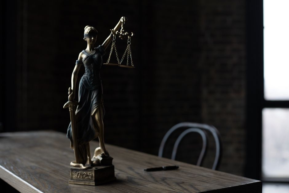 Estátua de justiça com balança sobre uma mesa de madeira, simbolizando imparcialidade e legislação.