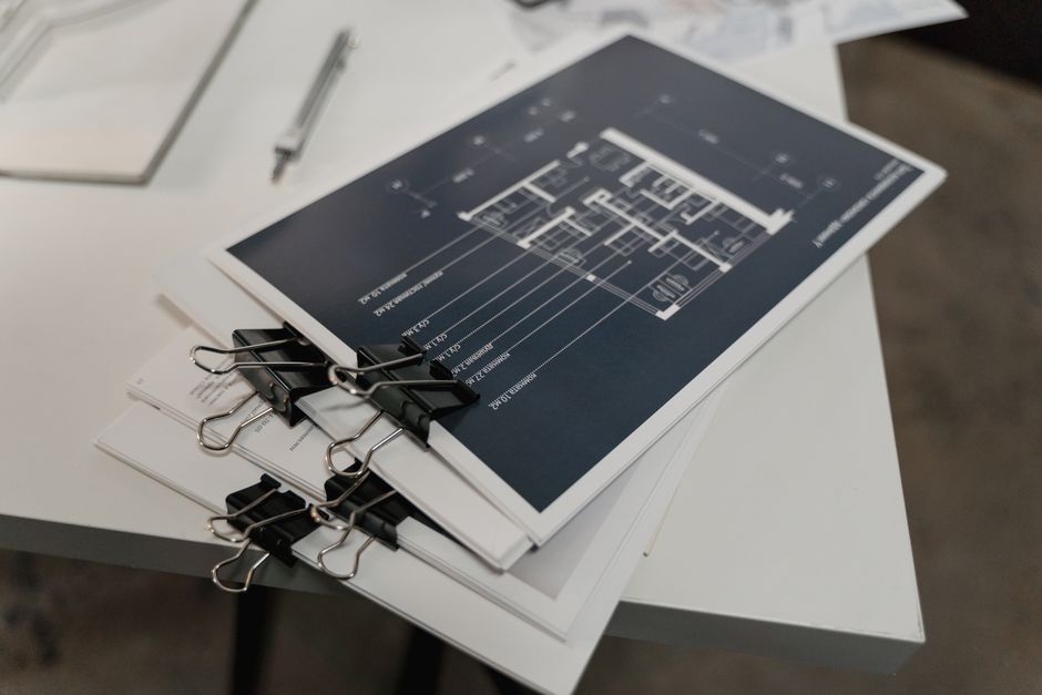 Imagem de uma mesa com documentos e uma planta arquitetônica presa com clipes, sugerindo planejamento e organização de projetos.