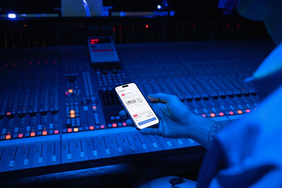 Pessoa controlando uma playlist de músicas usando um smartphone em uma sala de estúdio de gravação com equalizador e equipamentos de áudio.