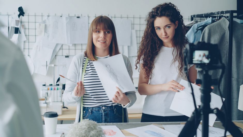 Duas jovens designeras realizando uma gravação de vídeo no estúdio, envolvendo trabalhos criativos e moda.