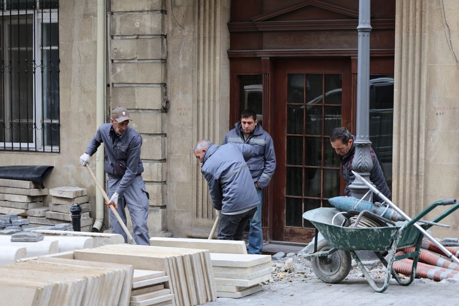 Homens trabalhando na reforma de uma fachada de prédio antigo na cidade, com materiais de construção ao redor.
