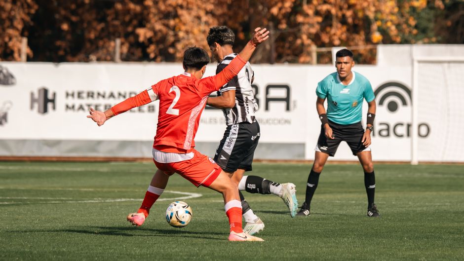 Ação de jogo de futebol com jogadores disputando a bola em um campo ao ar livre, durante uma partida animada