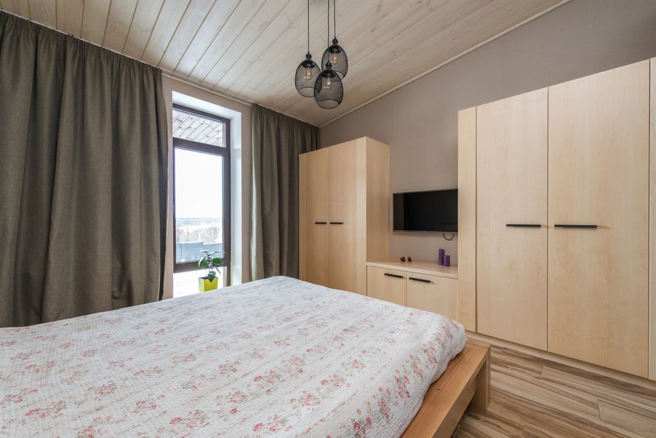 Quarto minimalista com móveis de madeira, varanda com cortinas pesadas e iluminação moderna.