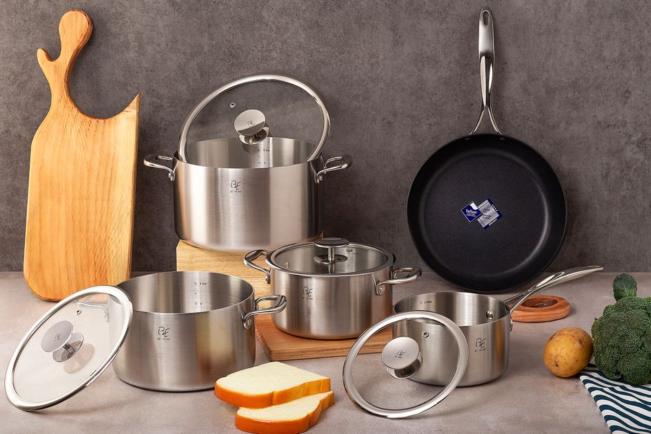 Imagem de panelas de aço inoxidável e utensílios de cozinha dispostos sobre uma bancada de cozinha moderna, destacando utensílios para preparo de alimentos.