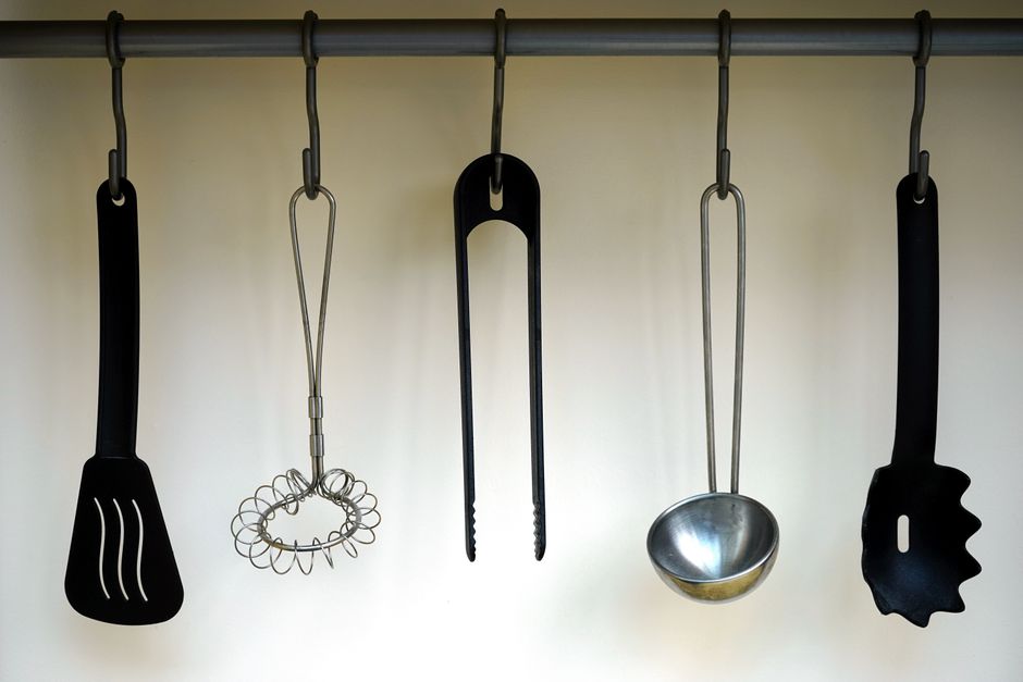 Ferramentas de cozinha penduradas em um suporte metálico, sugerindo organização e preparação culinária.
